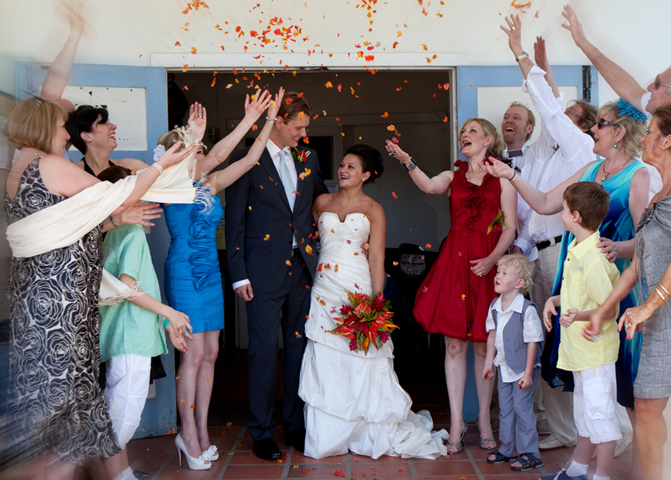 Newlyweds leaving their ceremony as guests toss colorful flower petals
