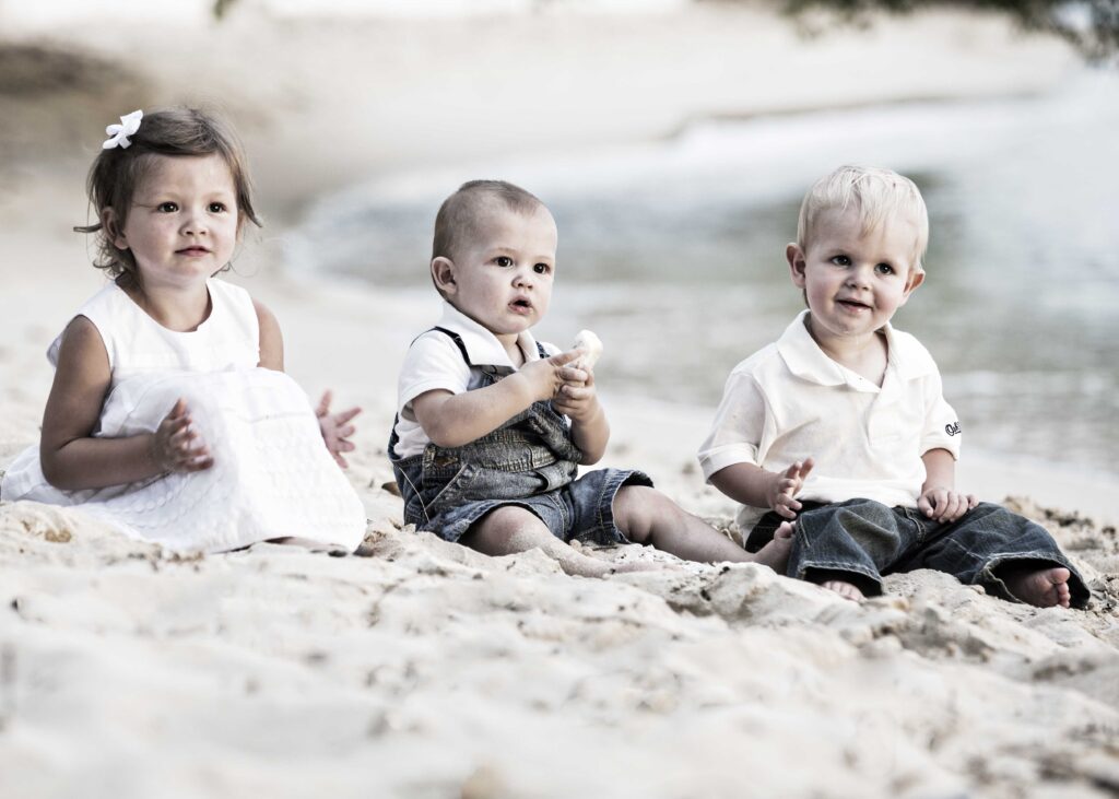 Three young children sitting together on a Barbados beach