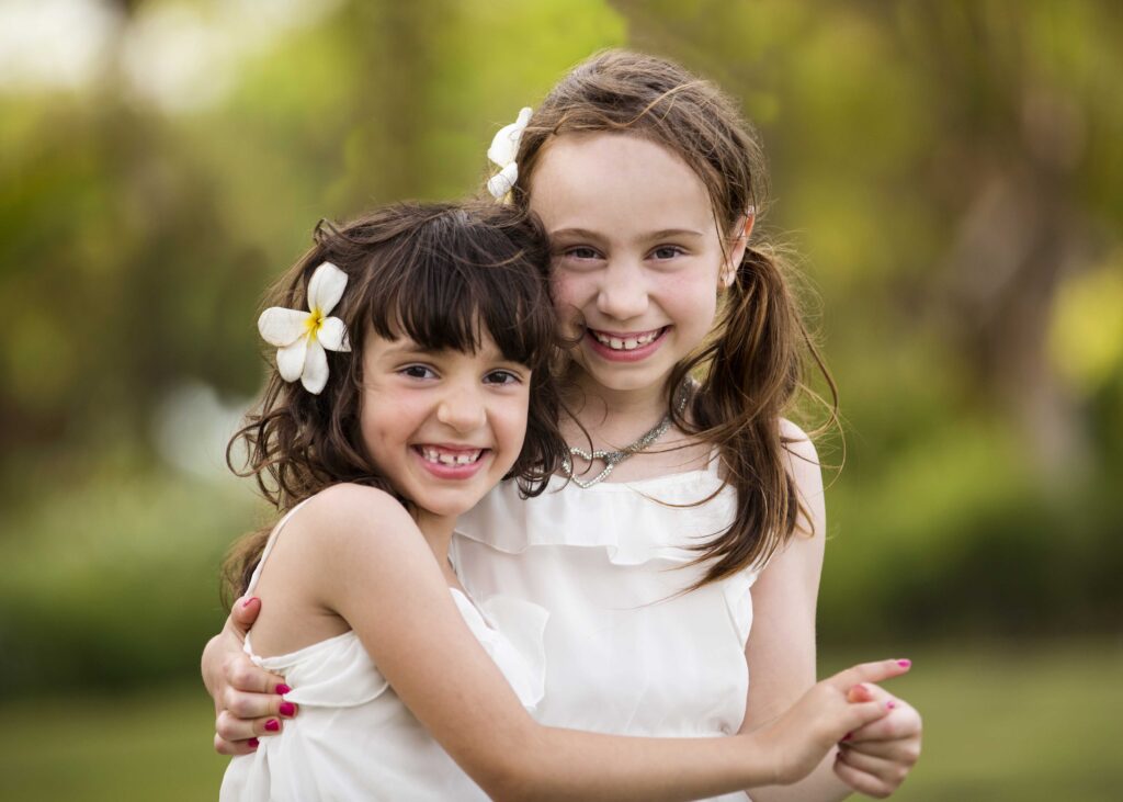 Two smiling girls embracing during an outdoor family portrait