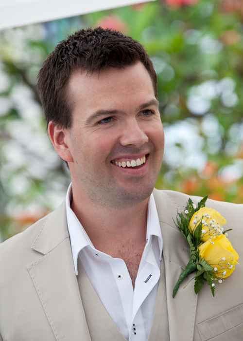 Smiling groom wearing a beige suit with a yellow rose boutonniere