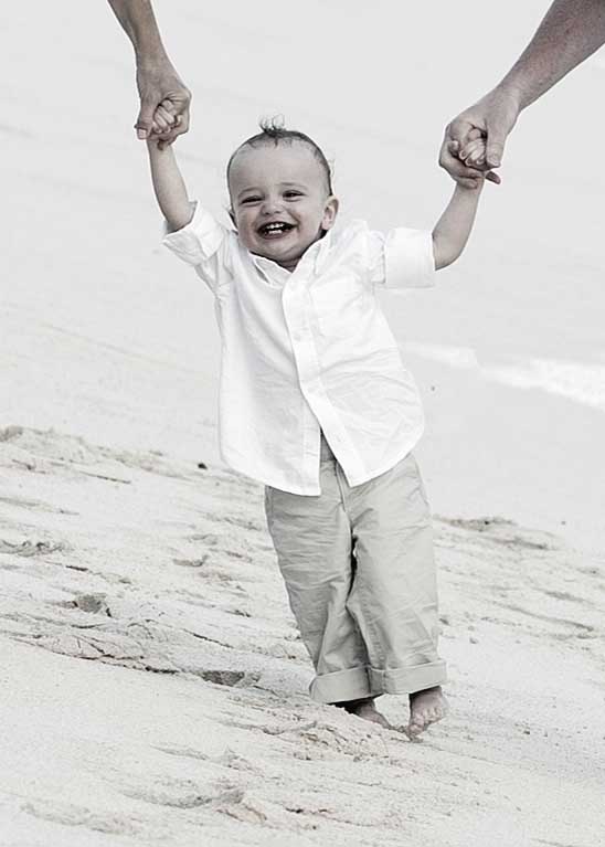 Smiling toddler walking on a Barbados beach while holding his parents' hands