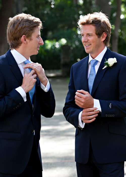 Groom adjusting his tie while speaking with a groomsman before the ceremony