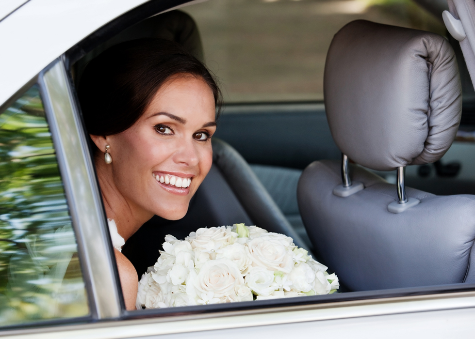 Smiling bride holding a white rose bouquet through the car window
