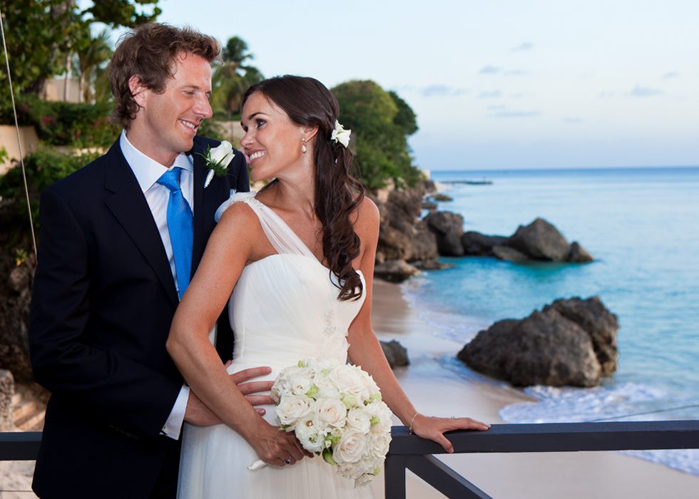Newlyweds smiling together above a rocky Barbados beach