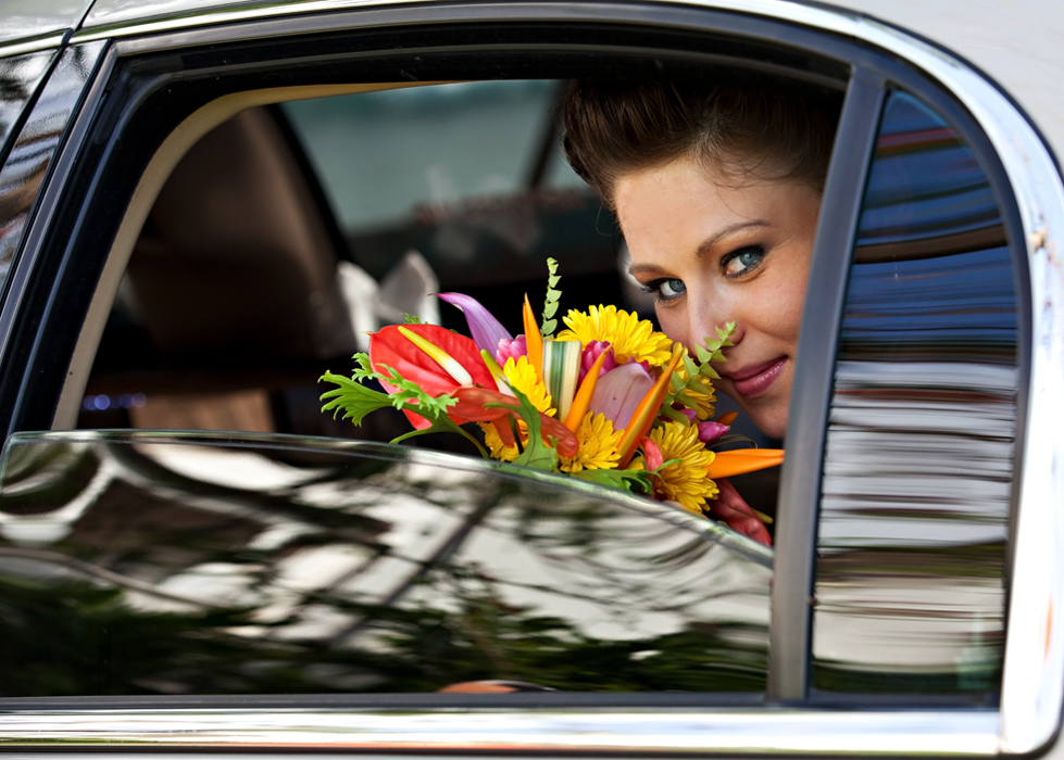 Bride holding a colorful tropical bouquet through the car window
