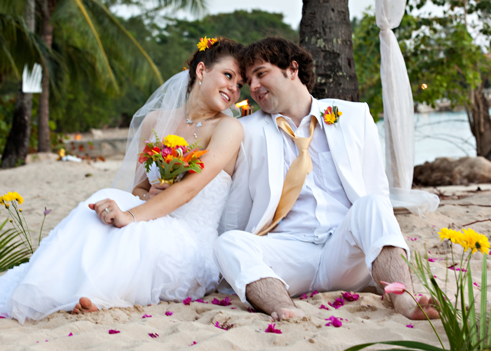 Newlyweds seated together on a Barbados beach with tropical flowers