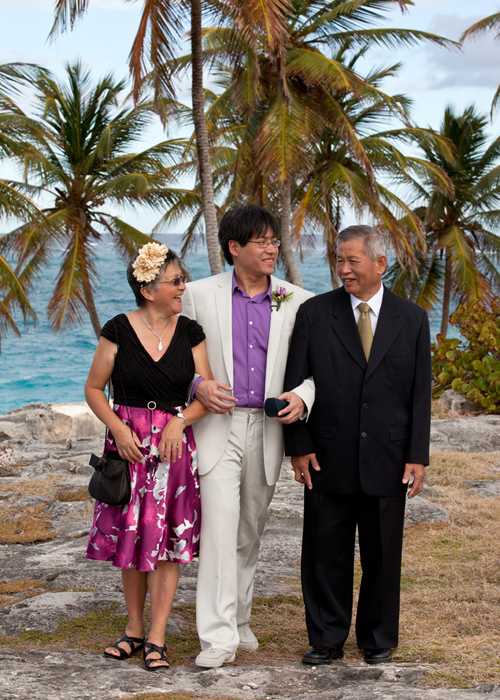 Groom walking with his parents beside palm trees before the ceremony