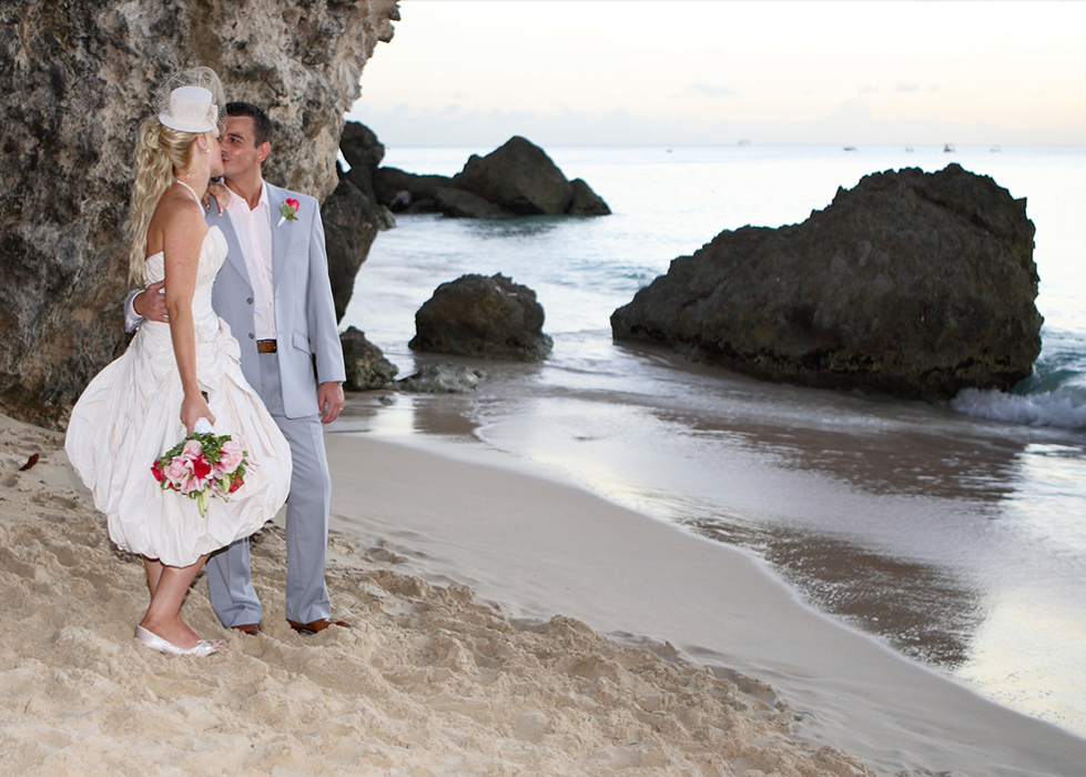 Bride and groom kissing on a rocky Barbados beach