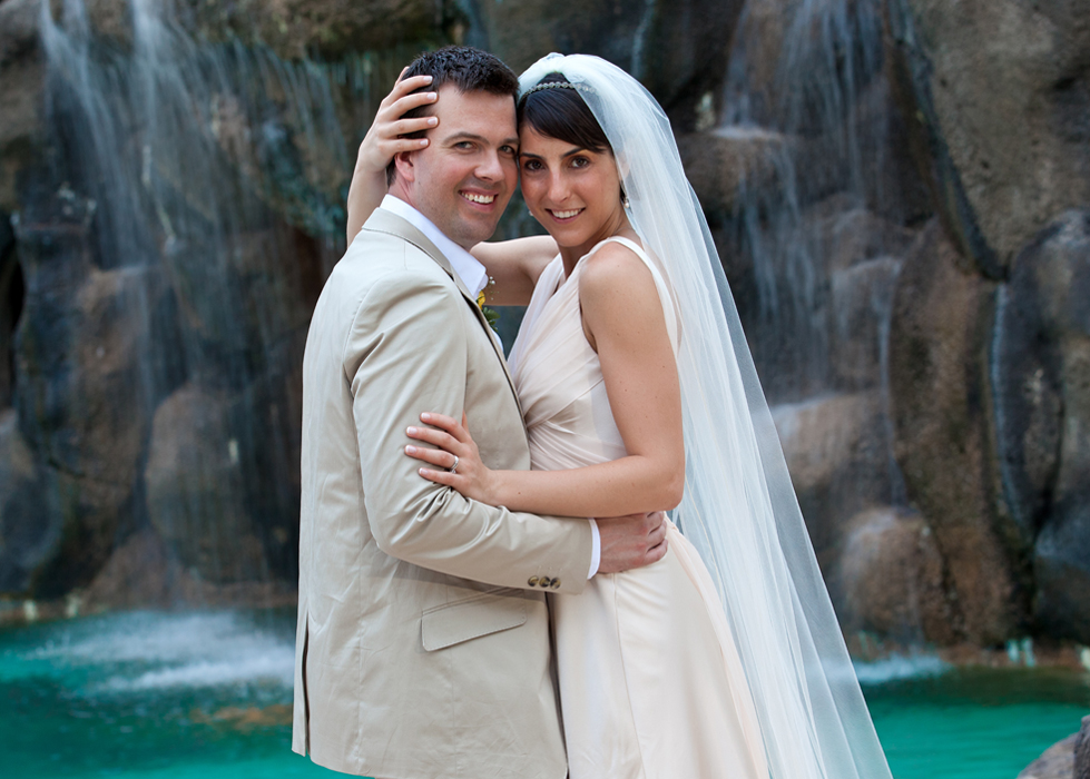 Bride and groom posing together beside a tropical waterfall