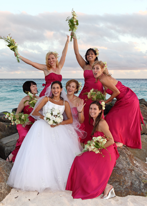 Bride celebrating with bridesmaids in bright pink dresses by the sea