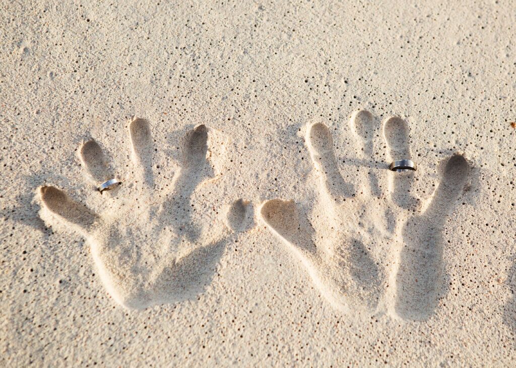 Family handprints and wedding rings pressed into Barbados beach sand