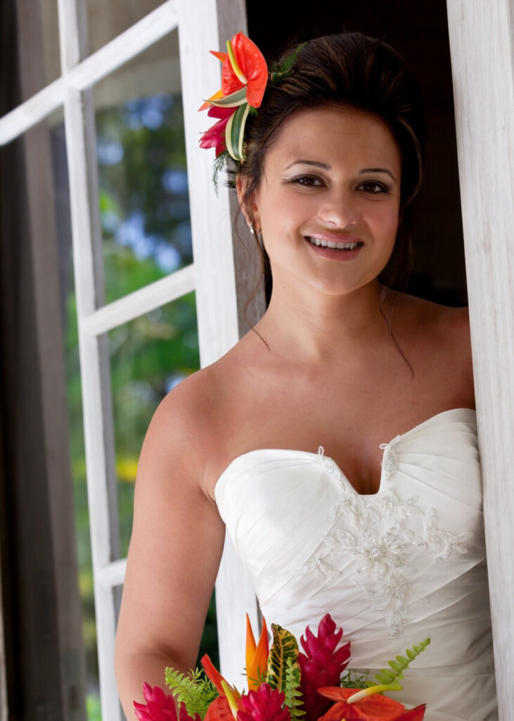 Bride holding tropical flowers beside a sunlit window