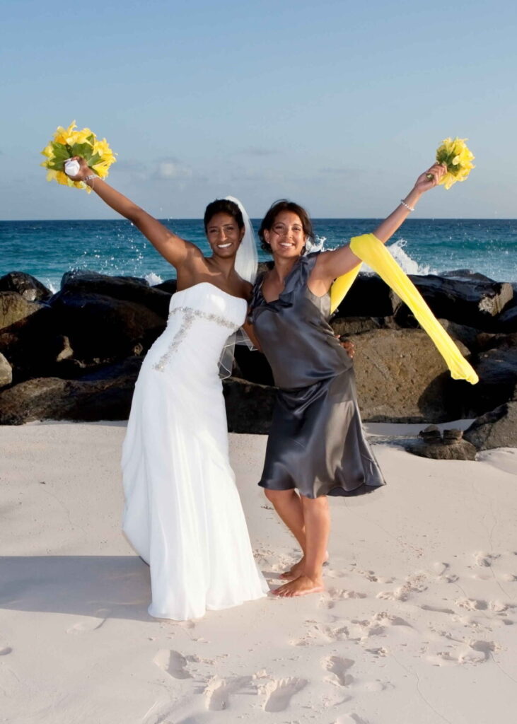 Bride celebrating with a bridesmaid beside the turquoise Barbados sea