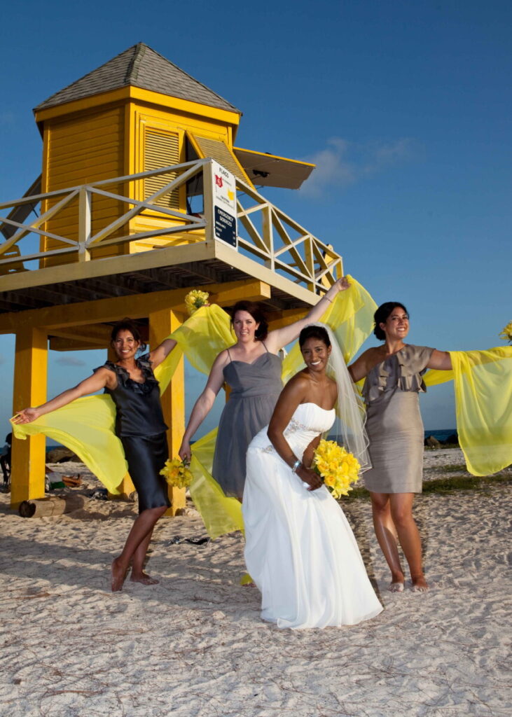 Bride and bridesmaids celebrating beside a yellow Barbados lifeguard tower